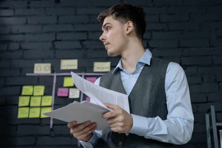 Een jonge mannelijke professional die projectdocumenten bestudeert in een moderne kantooromgeving met een takenbord.