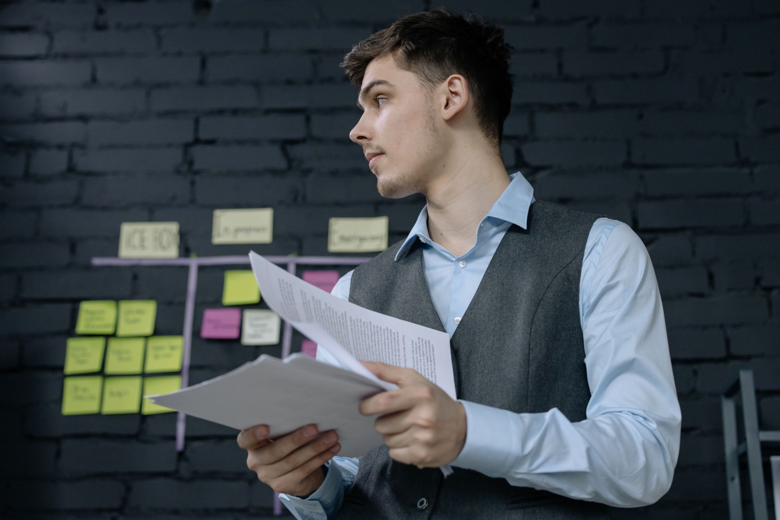 Een jonge mannelijke professional die projectdocumenten bestudeert in een moderne kantooromgeving met een takenbord.