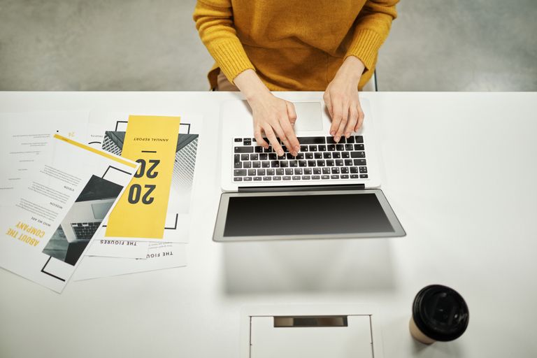Een vrouw in een gele trui die op een laptop werkt aan een modern, minimalistisch bureau.