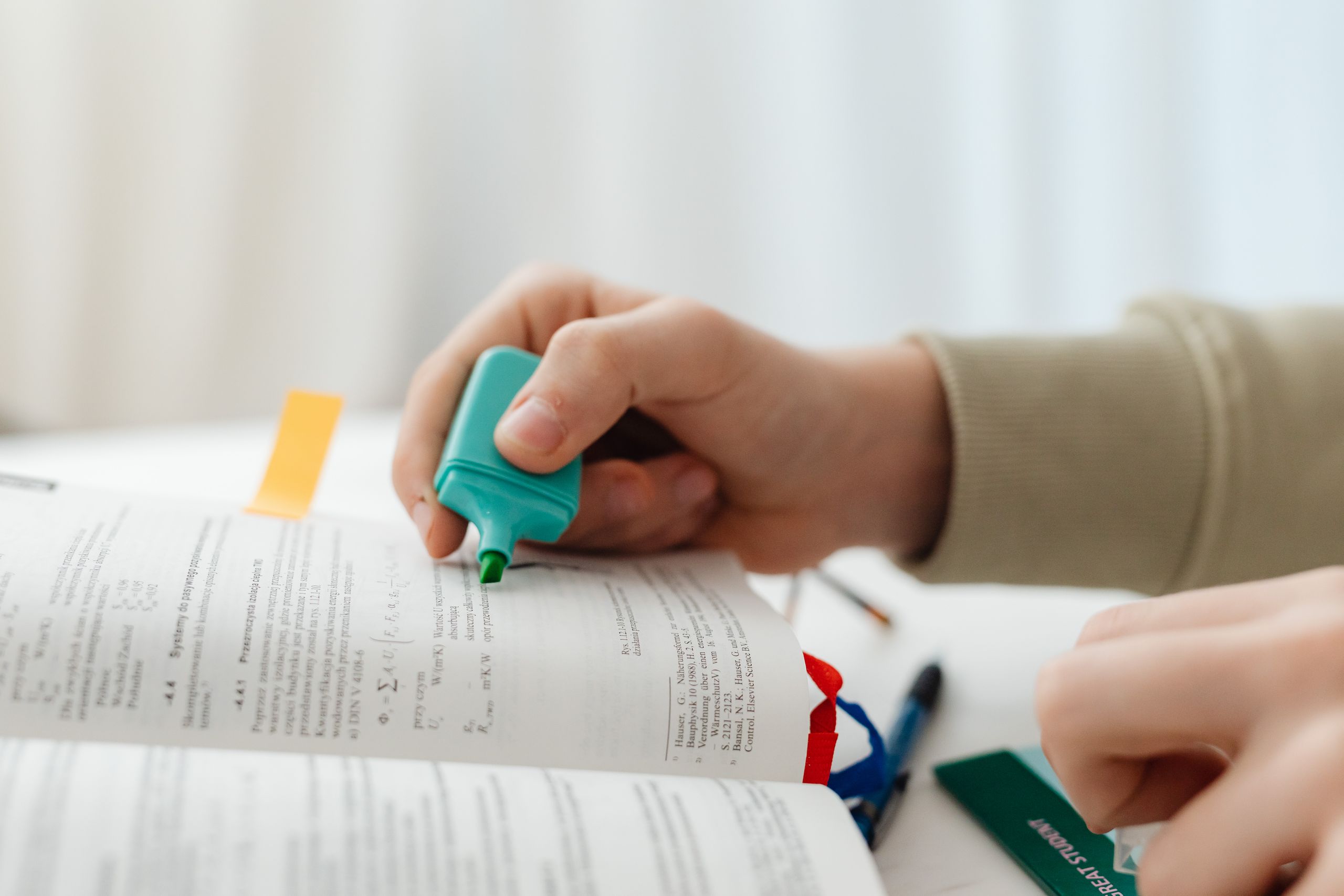Iemand die met een groene markeerstift tekst in een boek markeert, een moment waarop hij geconcentreerd aan het studeren is.